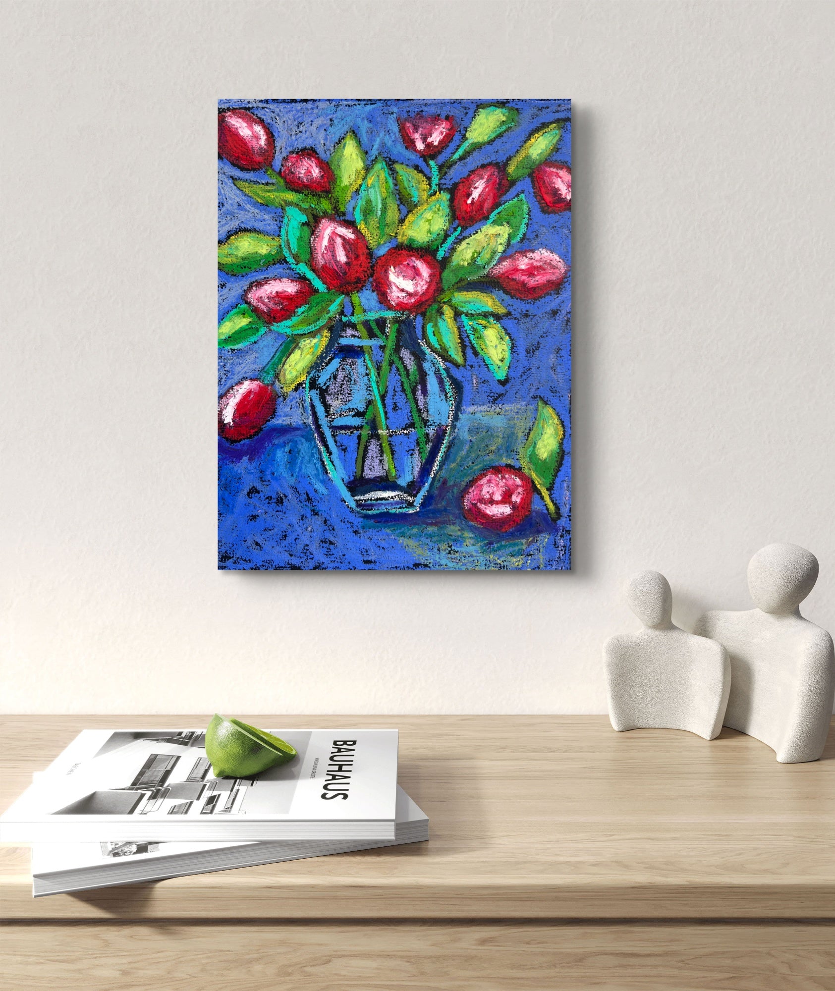 Colorful painting of flowers in a vase on a wall above a table with magazines and decorative items.