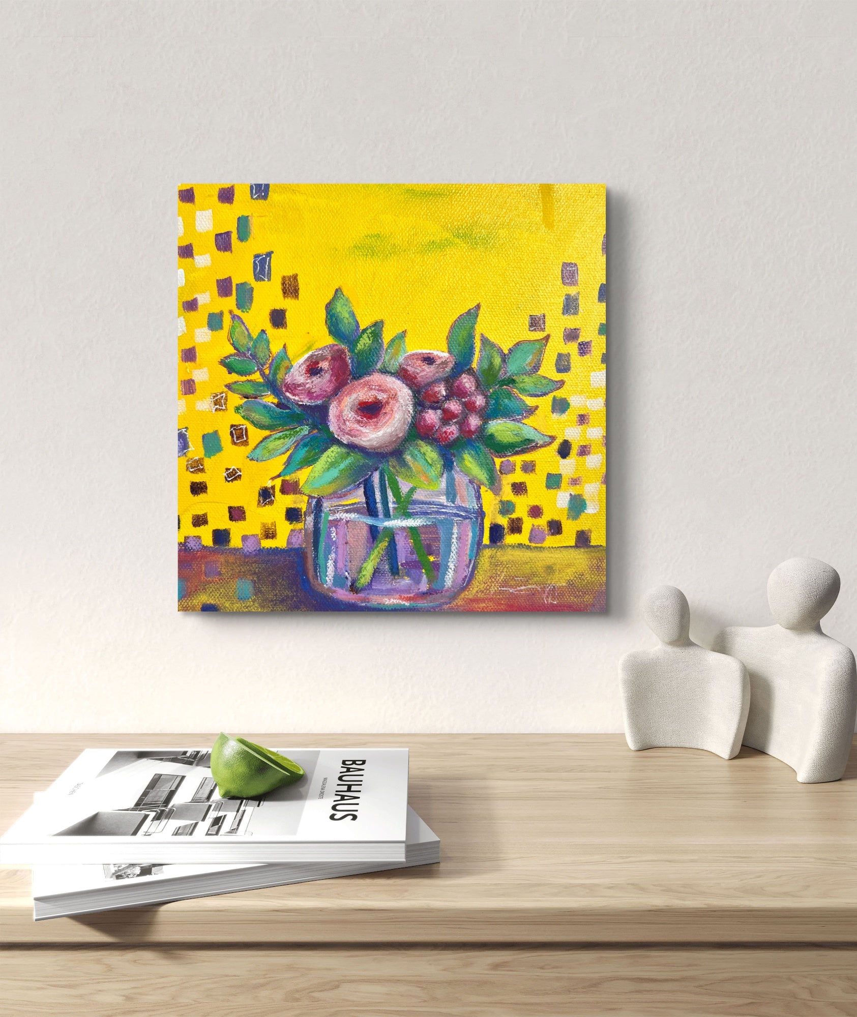 Colorful floral painting on a wall above a wooden table with magazines and decorative items.