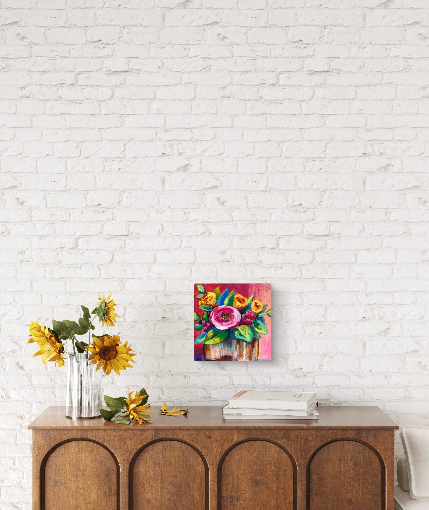 Colorful floral painting on a white brick wall above a wooden console table with sunflowers.